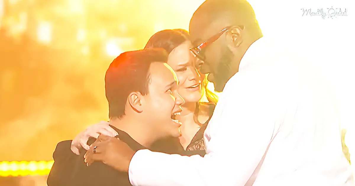 A man in white embraces another man, both smiling, with a bright, golden background.