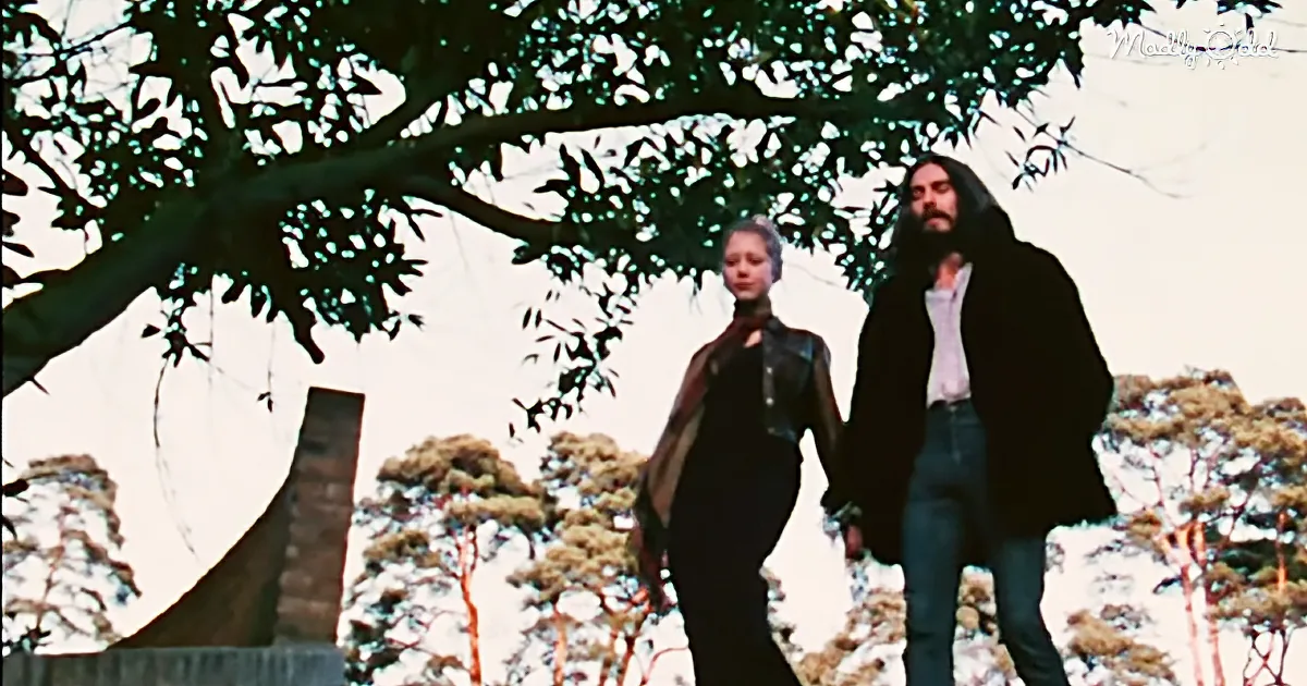 A couple walks hand in hand under a tree, surrounded by nature.
