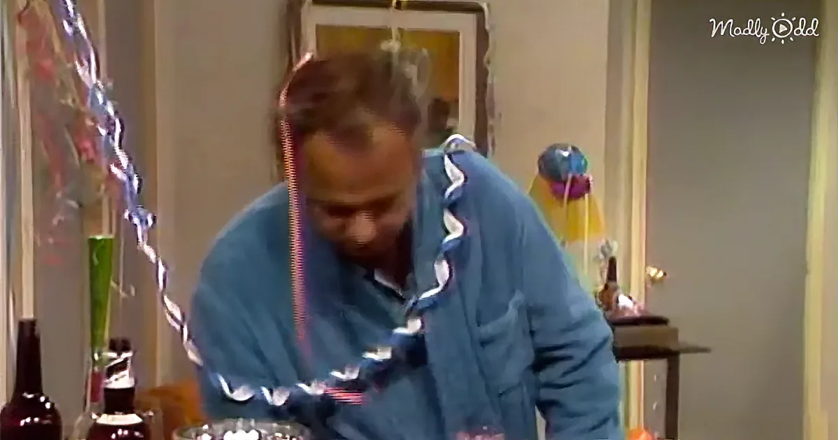 A man in a blue shirt is bent over, looking at something on a table with bottles and decorations around.