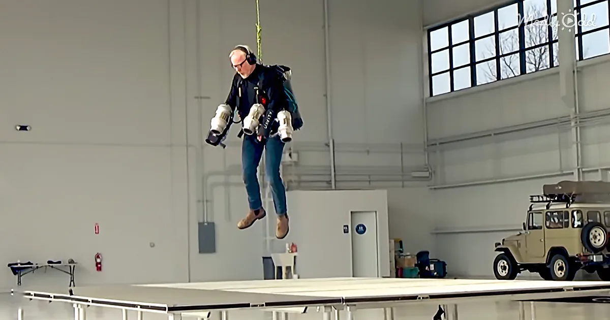 A man wearing a jetpack is suspended mid-air in a large indoor space.