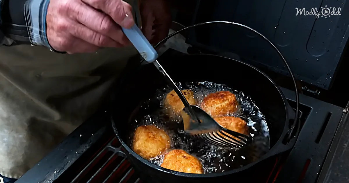 A person uses a fork to flip golden-brown fried food in a black cast iron skillet on a grill.