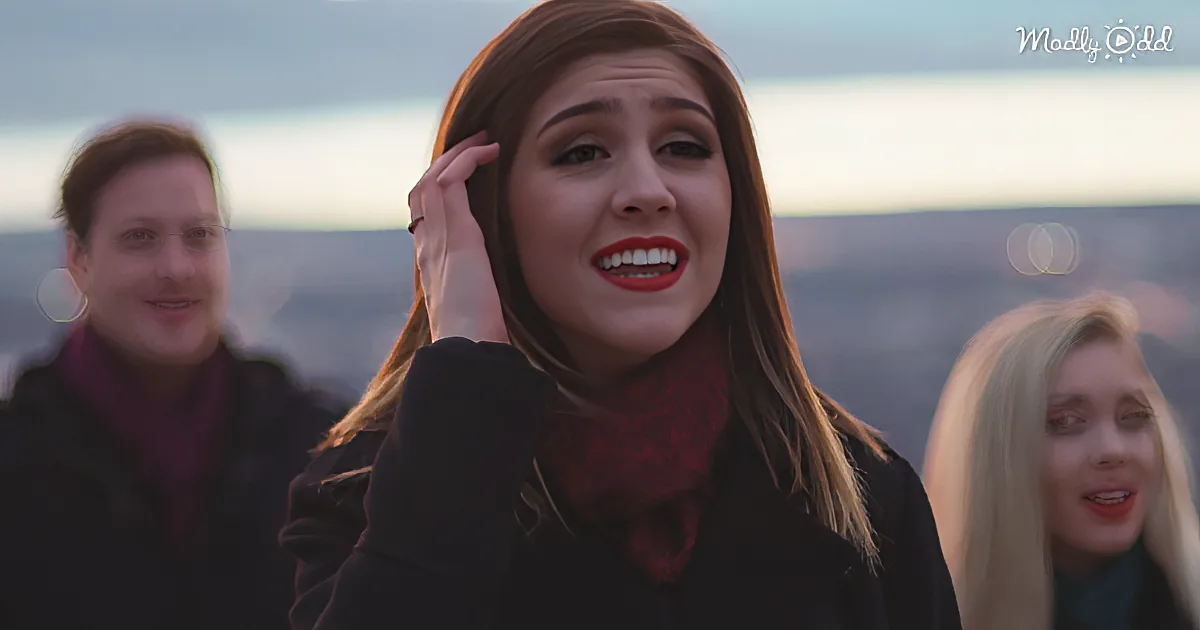 A woman with red lipstick and a red scarf adjusts her hair, smiling, with two blurred figures behind her.