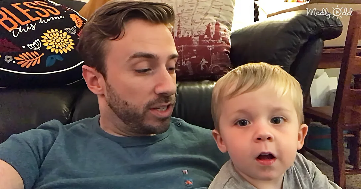 A man and a young child are sitting together, with the man speaking and the child looking up.