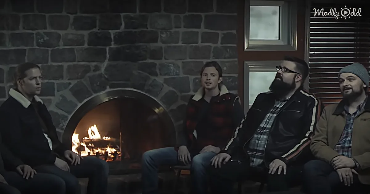 Four men sit in front of a stone fireplace, engaged in conversation, with one man speaking.