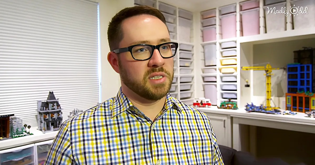 A man in a yellow and blue checkered shirt stands in front of shelves filled with LEGO models and storage bins.