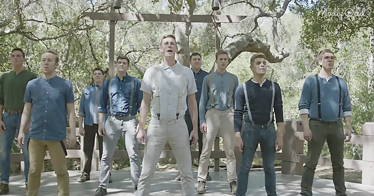 A man in a white shirt and suspenders leads a group of men in a synchronized dance on a wooden bridge.