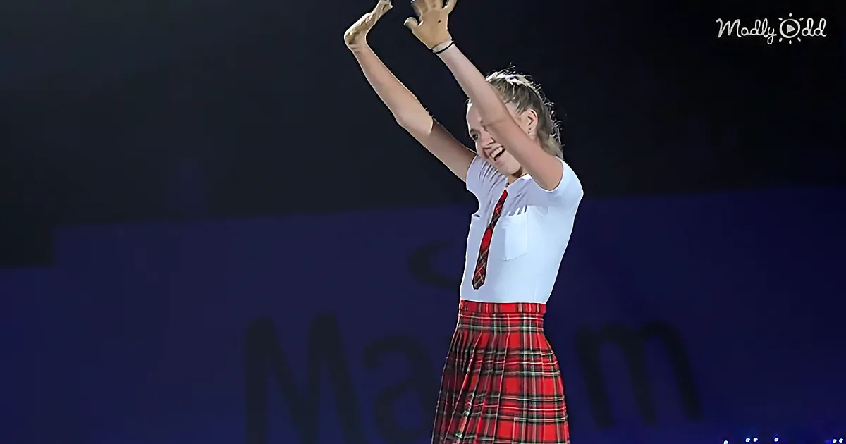A person in a white shirt and red plaid skirt raises their arms in celebration, smiling widely.