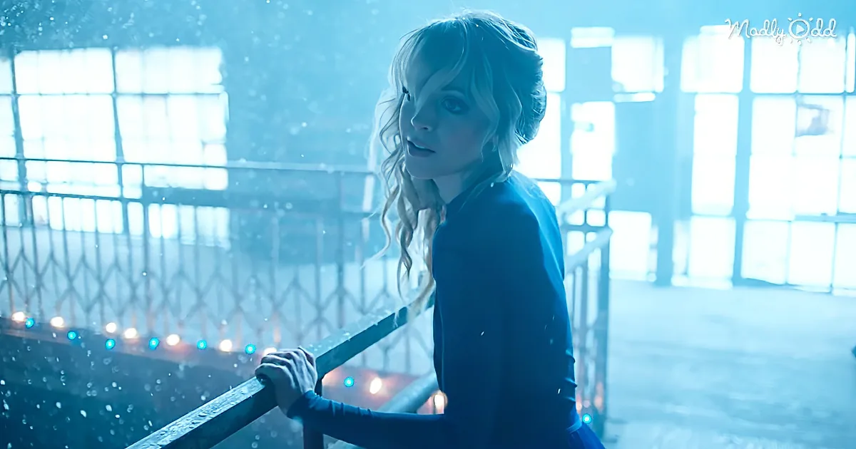 A woman with curly hair leans on a railing, looking back with a surprised expression in a dimly lit, snowy environment.