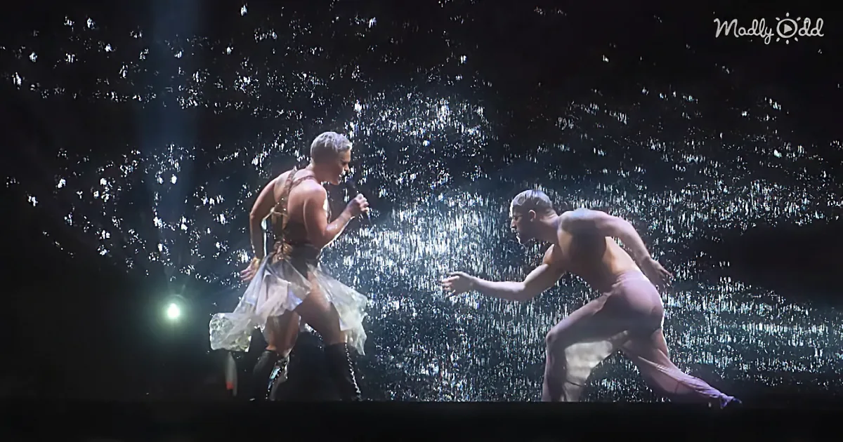 A performer in a white outfit sings into a microphone, accompanied by a dancer in a crouched position.