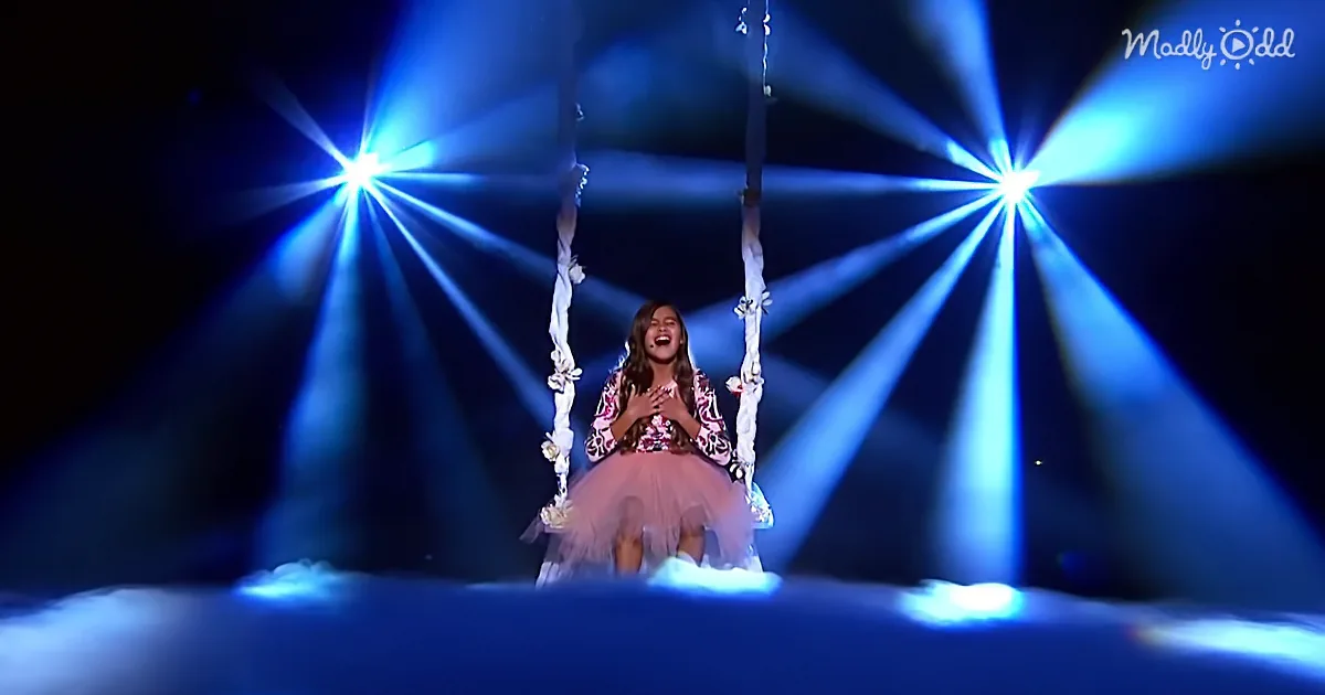 A person swings on a swing with a pink tutu and floral jacket, surrounded by blue stage lights.