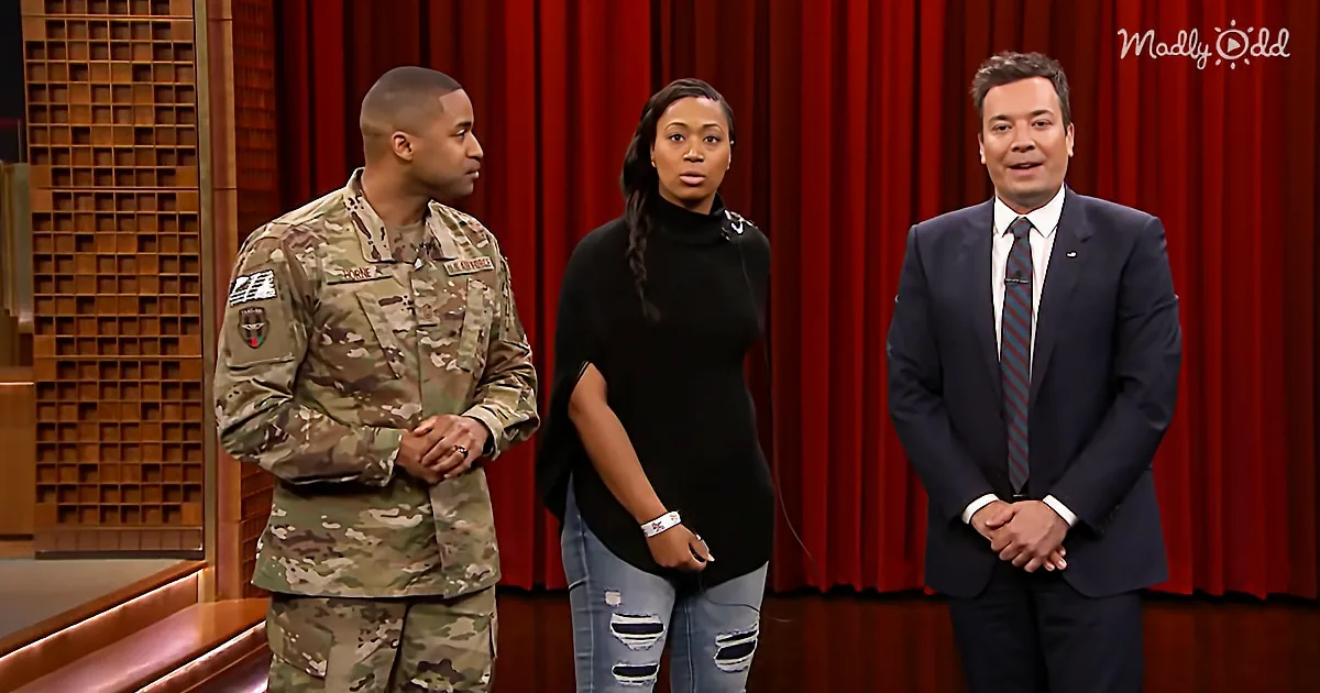 A man in military uniform stands next to a woman in a black top and jeans, with a man in a suit on the right.