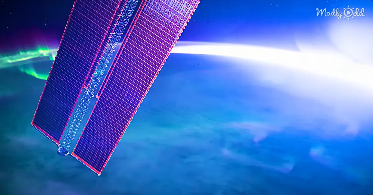 A satellite with solar panels is seen against a backdrop of Earth's atmosphere and aurora.