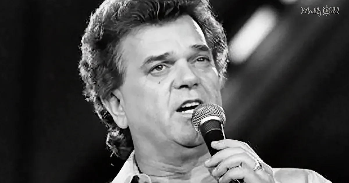 A man with curly hair sings into a microphone, wearing a light-colored shirt.