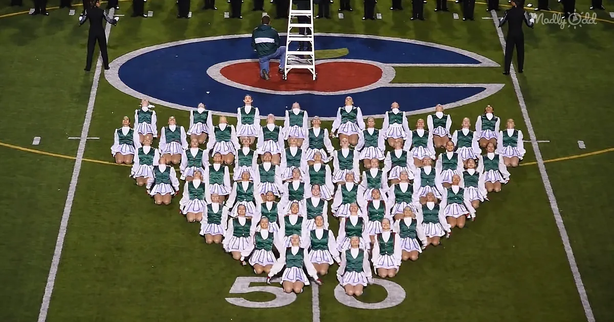 Cheerleaders in green and white uniforms form a heart shape on a football field.