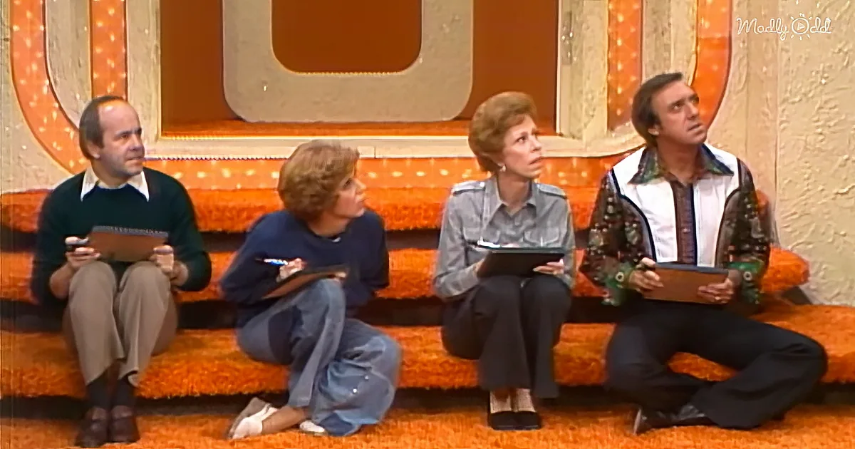 Four people sit on an orange couch, holding clipboards, in a retro studio setting.