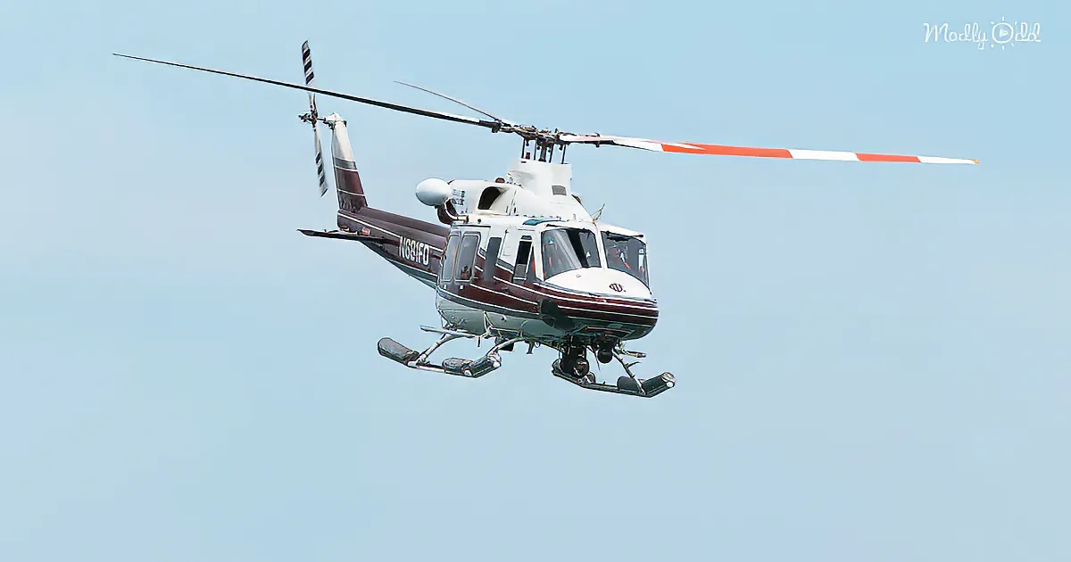A Bell helicopter with red and white tail blades is flying against a clear sky.