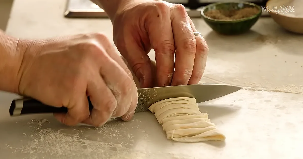 Hands slicing dough with a knife on a floured surface.