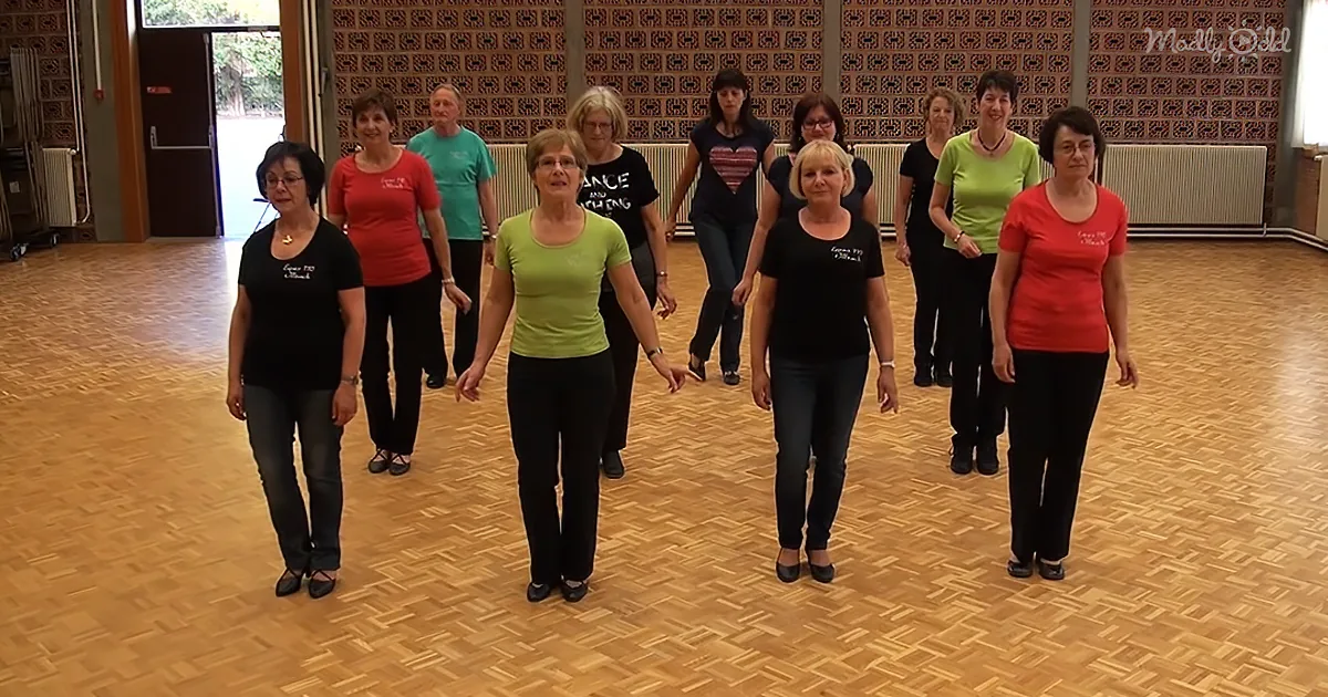 A group of women in a dance studio, standing in a line, wearing casual attire.
