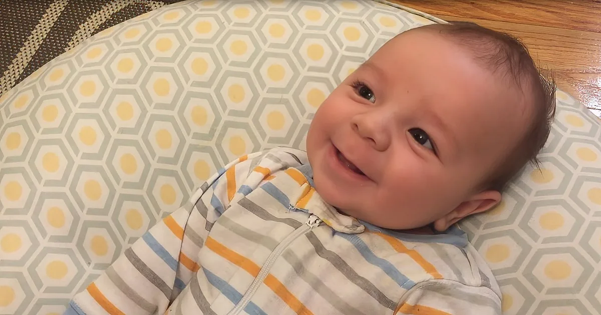 A baby in striped pajamas smiles while lying on a hexagonal-patterned pillow.