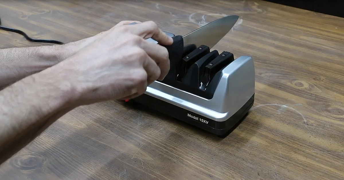 A hand holds a knife being sharpened on a Model 15XV electric sharpener.