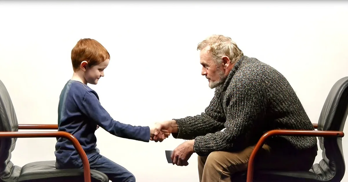 A young boy and an older man are shaking hands while seated in chairs.