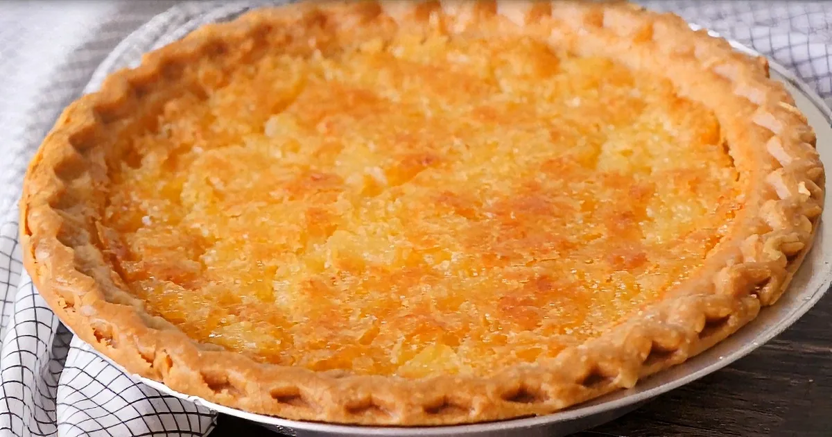 A golden-brown pie with a flaky crust sits on a white plate, ready to be served.