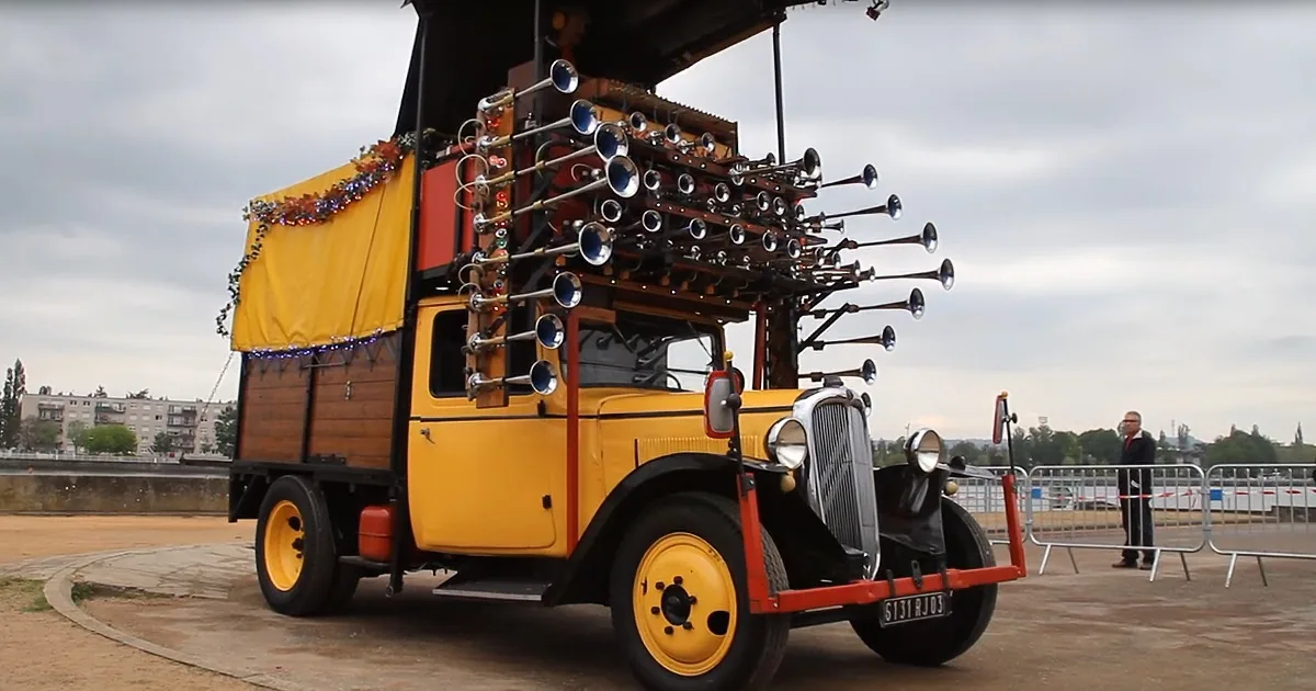 A vintage yellow truck adorned with colorful decorations and multiple horns is parked outdoors.