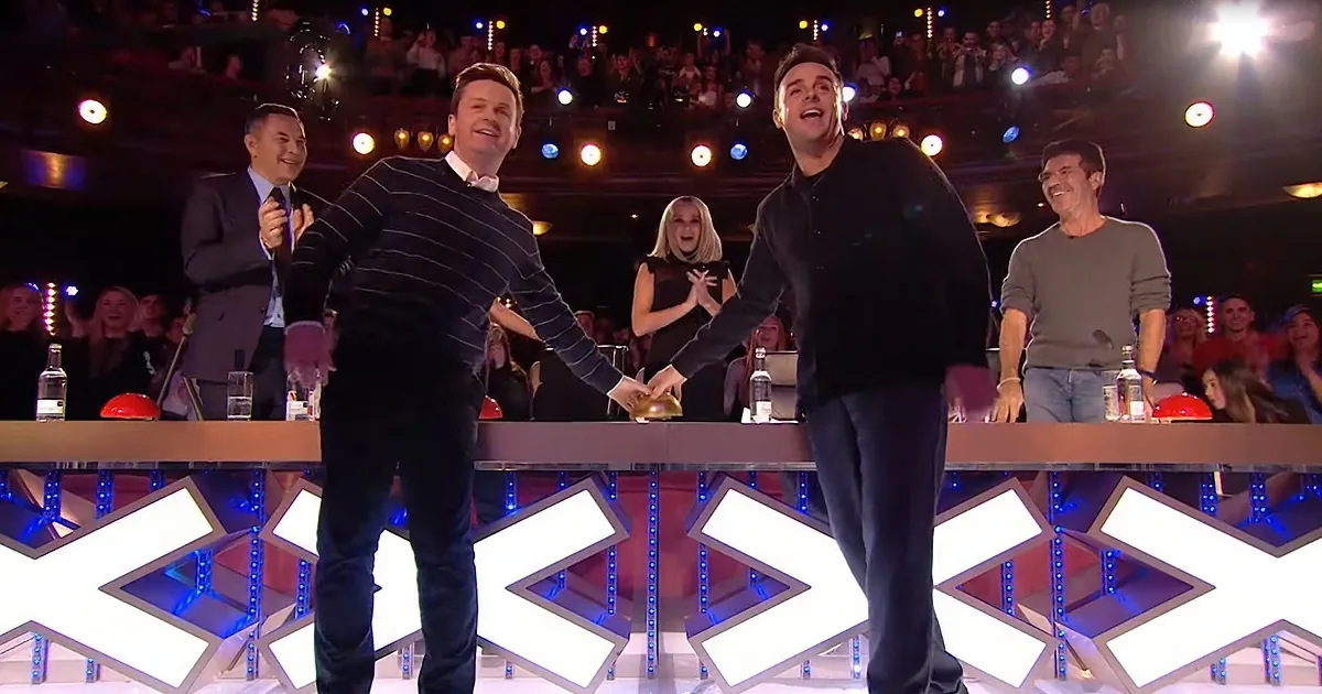 Two men are shaking hands on a stage with a cheering audience and judges in the background.