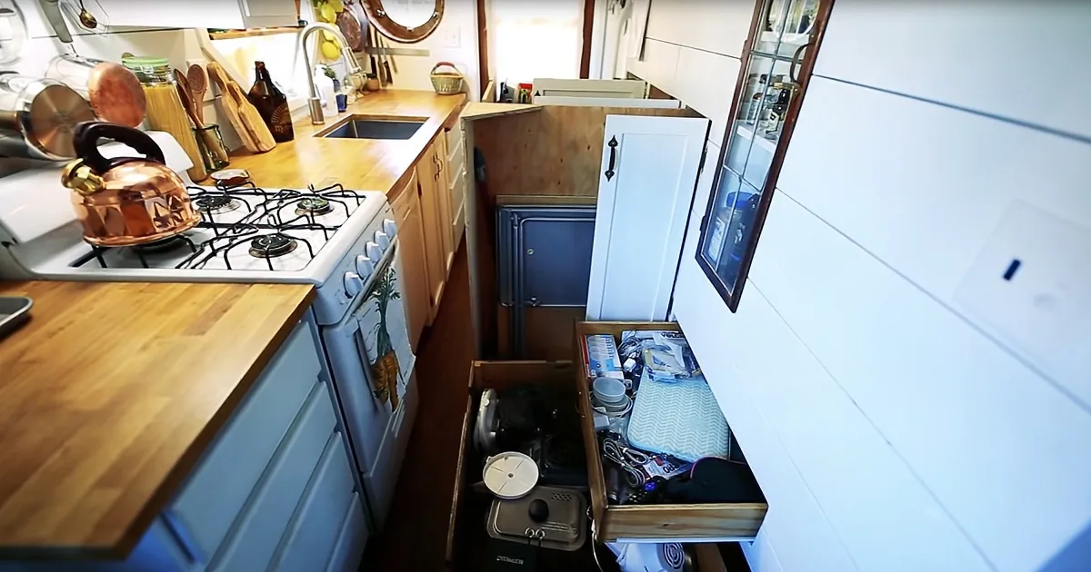 A compact kitchen with a copper kettle on a gas stove, wooden countertops, and a small storage area under the counter.
