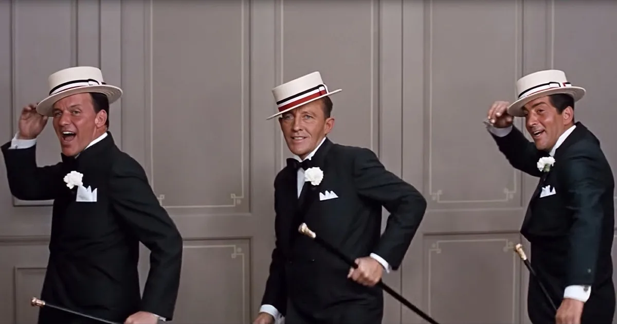 Three men in tuxedos and top hats are dancing and laughing, holding canes.