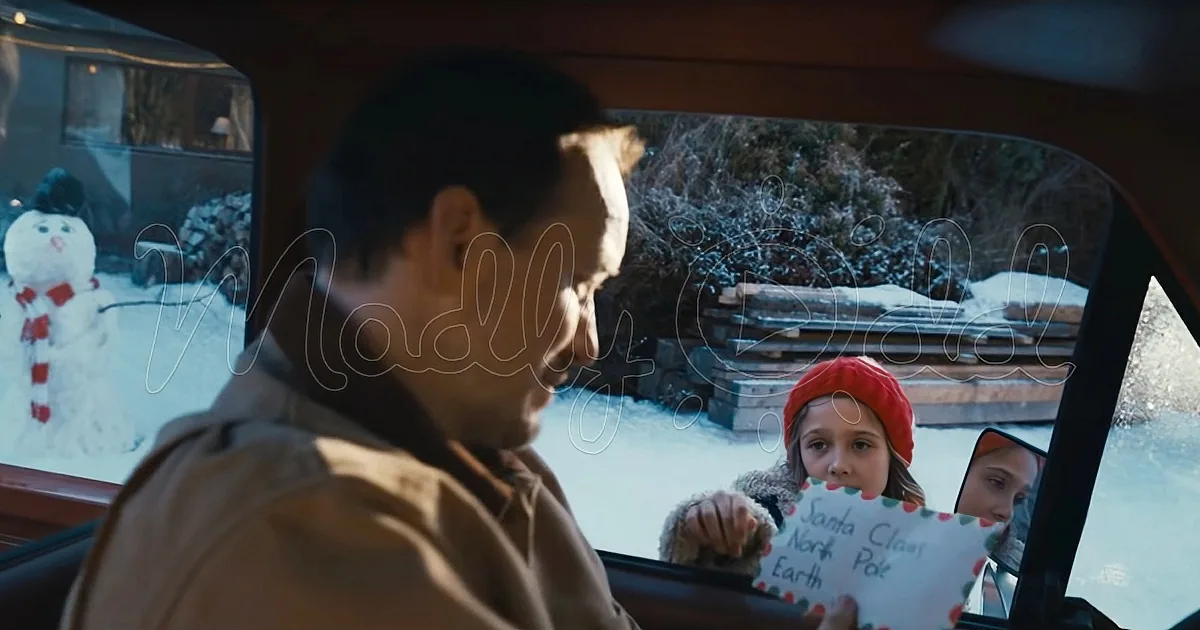 A man in a car looks at a child holding a letter to Santa Claus.
