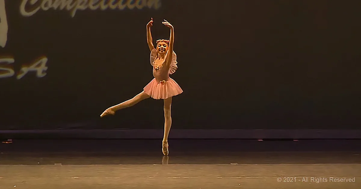 A ballerina in a pink tutu and white leotard performs a graceful pose on stage.