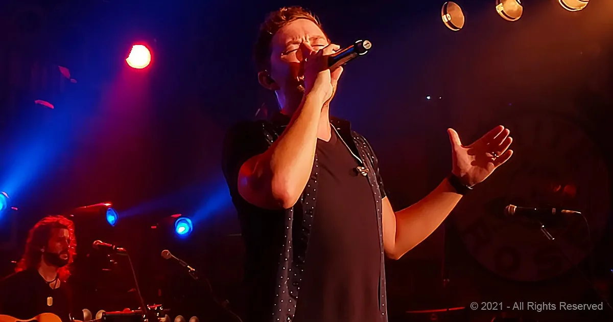 A singer passionately performs on stage with a microphone, surrounded by colorful stage lights.