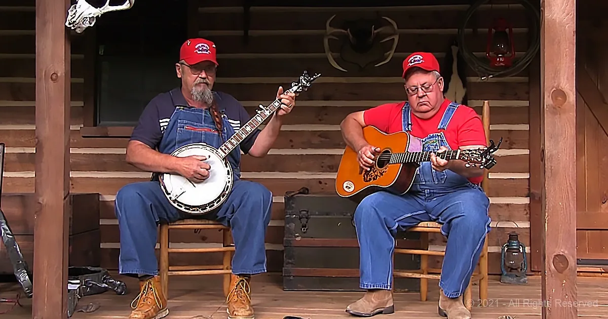 Two men in overalls play banjo and guitar on a rustic porch.