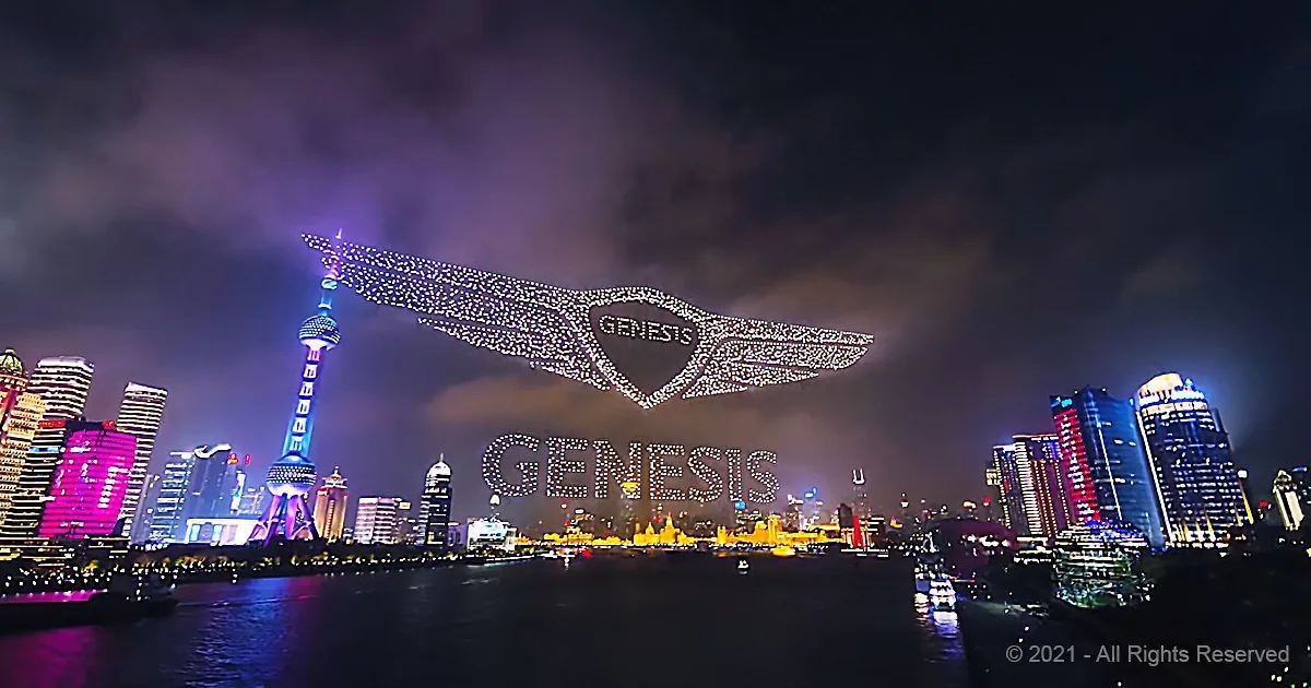A massive illuminated Genesis logo with wings spans the night sky over a cityscape.