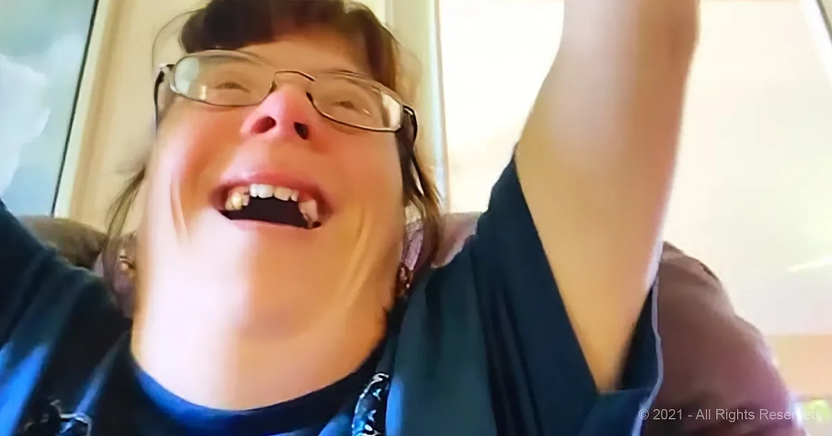 A person wearing glasses and a dark shirt is smiling widely with their arms raised.