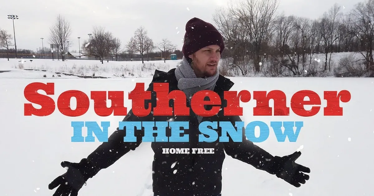 A man in a winter outfit stands in a snowy field, arms outstretched, looking to the side.