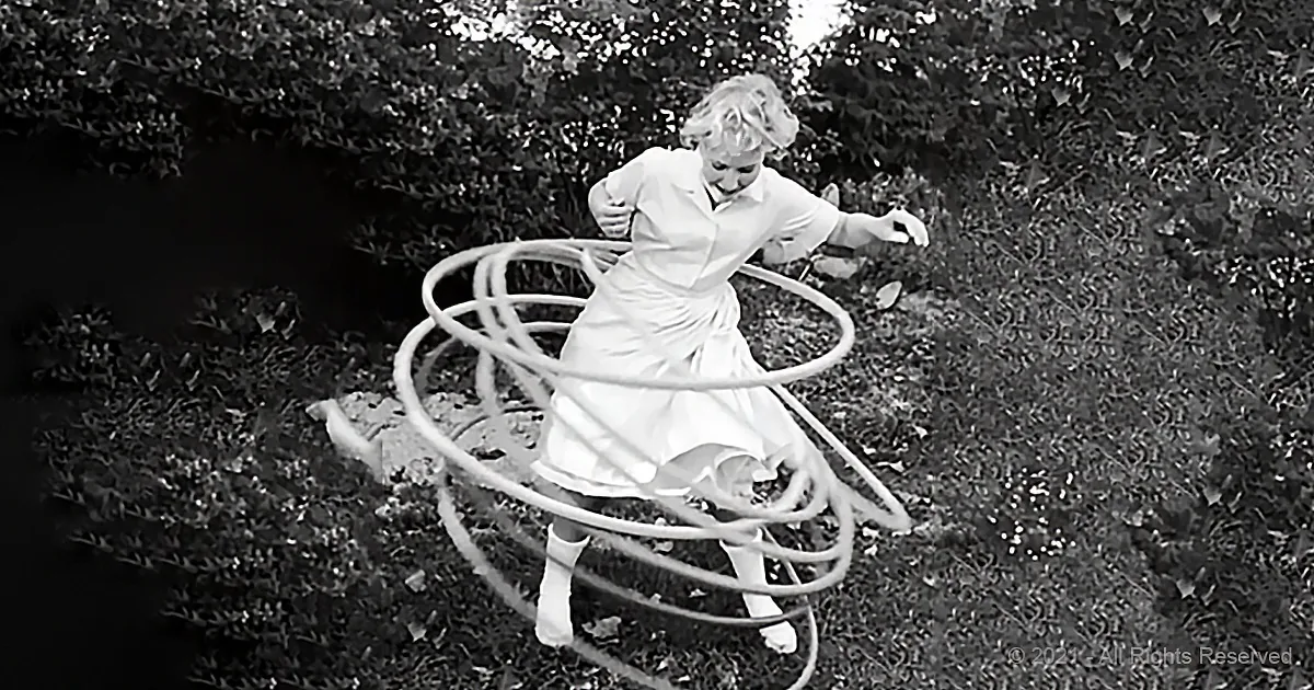 A woman in a white dress is surrounded by multiple hula hoops in a grassy area.