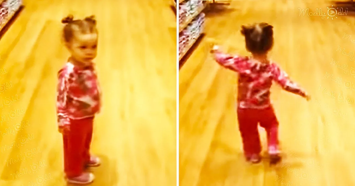 A young child in a red outfit stands on a yellow floor, then turns and walks away.