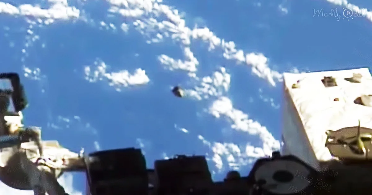 A small object, possibly a satellite or drone, is seen flying against a backdrop of blue sky and scattered clouds.