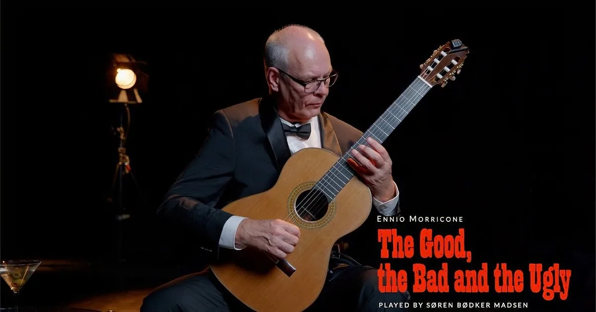 An older man in a tuxedo plays a classical guitar in a dimly lit setting.