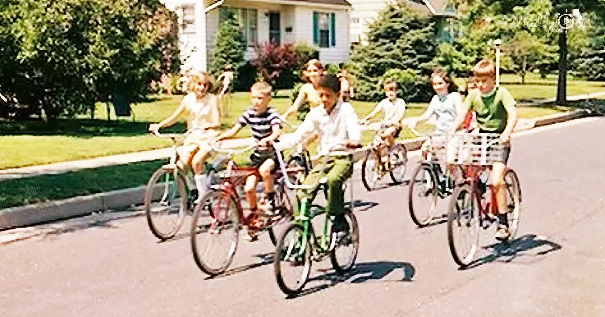 Six children riding bicycles in a line on a suburban street.