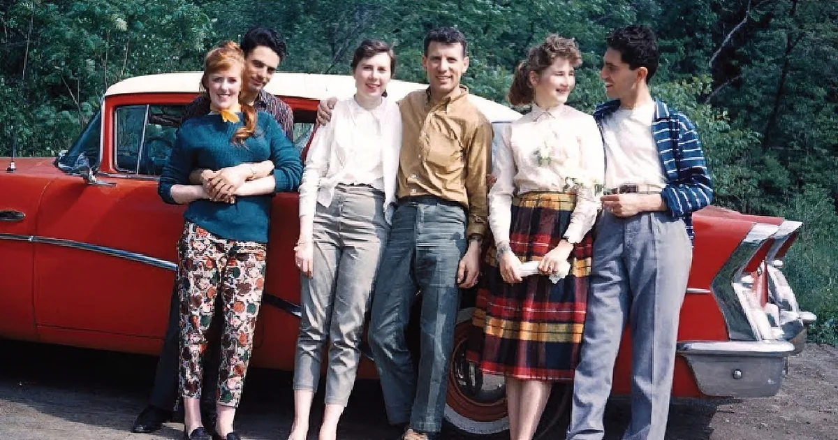 A woman and two children smile from the windows of a vintage teal car.
