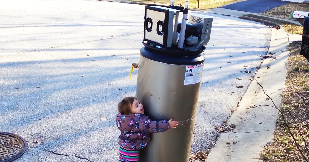 A toddler hugs a large water heater on a sunny sidewalk.