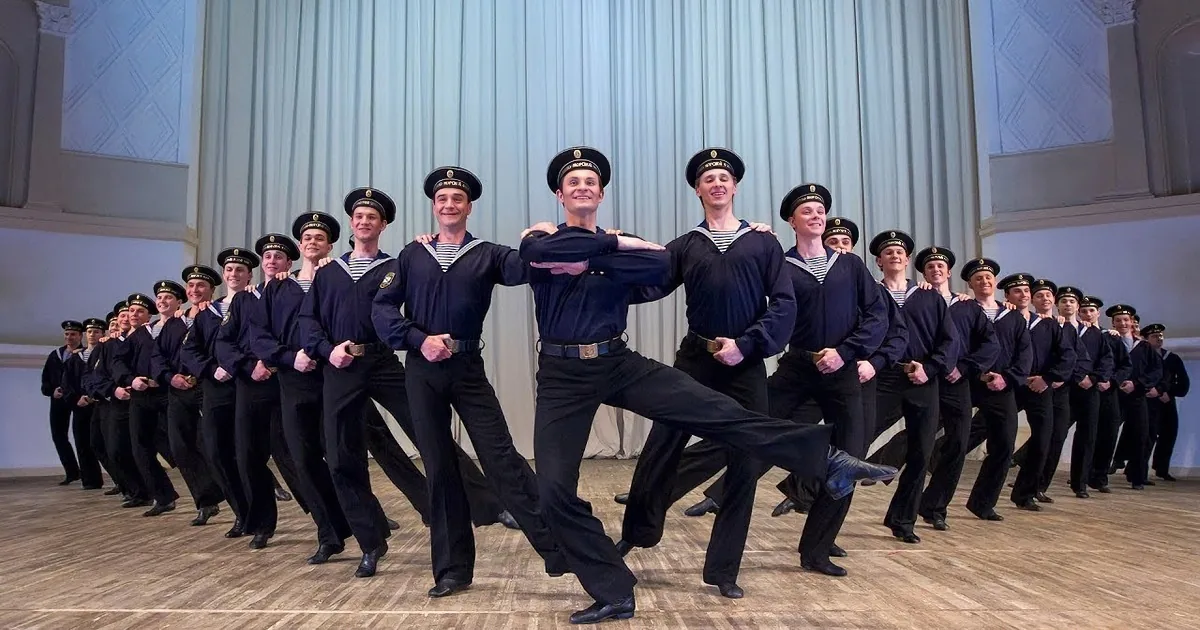 A group of performers in navy uniforms execute a synchronized dance routine on stage.