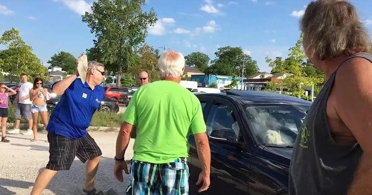 A man in a blue shirt is aggressively pointing a gun at another man in a green shirt.