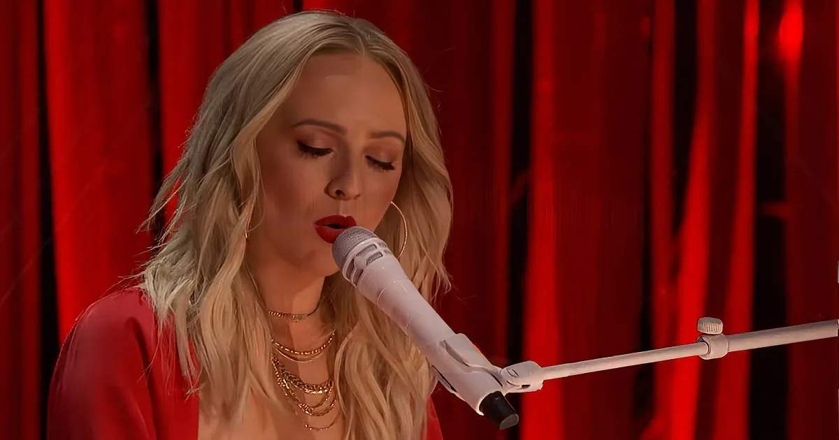A woman with blonde hair and red lipstick sings into a microphone against a red curtain backdrop.