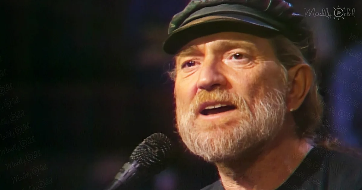 An older man with a beard and hat sings into a microphone, wearing a dark shirt.