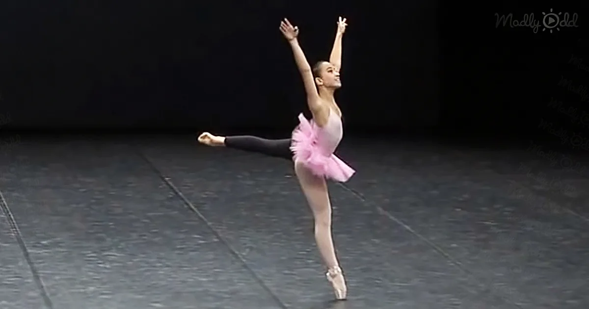 A ballerina in a pink tutu and black tights performs a graceful pose on stage.