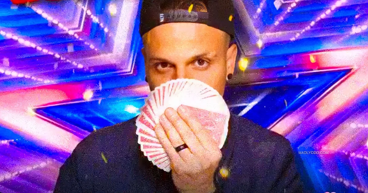 A man in a black outfit holds a fan of cards in front of his face, with a colorful, illuminated background.